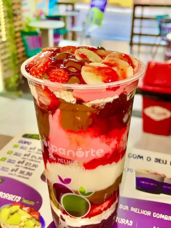 Copo de açaí visto de lado, com camadas de açaí, creme, morango e chocolate