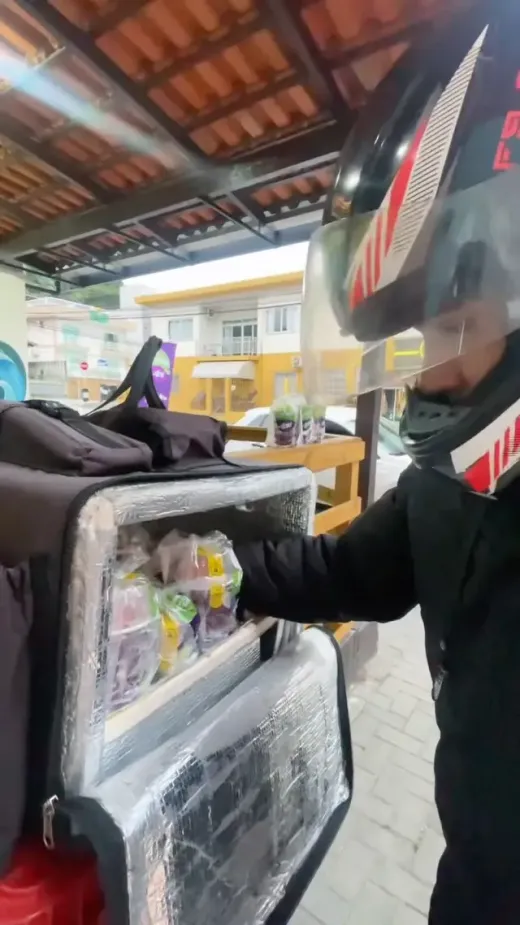 Entregador abrindo a bag térmica do delivery com pedidos da Labele
