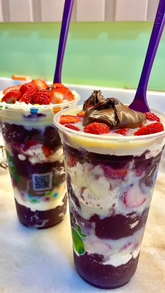 Dois copos de açaí com morango, creme e chocolate no balcão